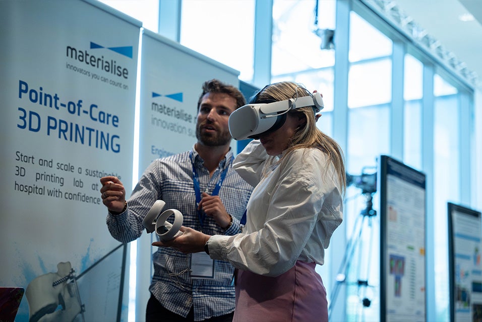 A 3D Printing in Hospitals Forum 2024 attendee trying out a VR headset with the assistance of a Materialise employee