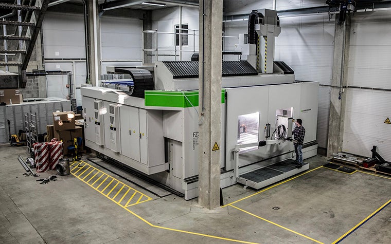Worker looking through a window into a huge CNC milling machine, while operating it via a screen 
