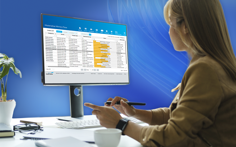 Woman sitting at a desk and looking at patient cases in Mimics Flow software with blue swirly lines in the background