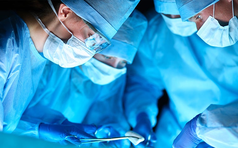 A group of surgeons in scrubs in the OR leaning over a patient with their tools ready