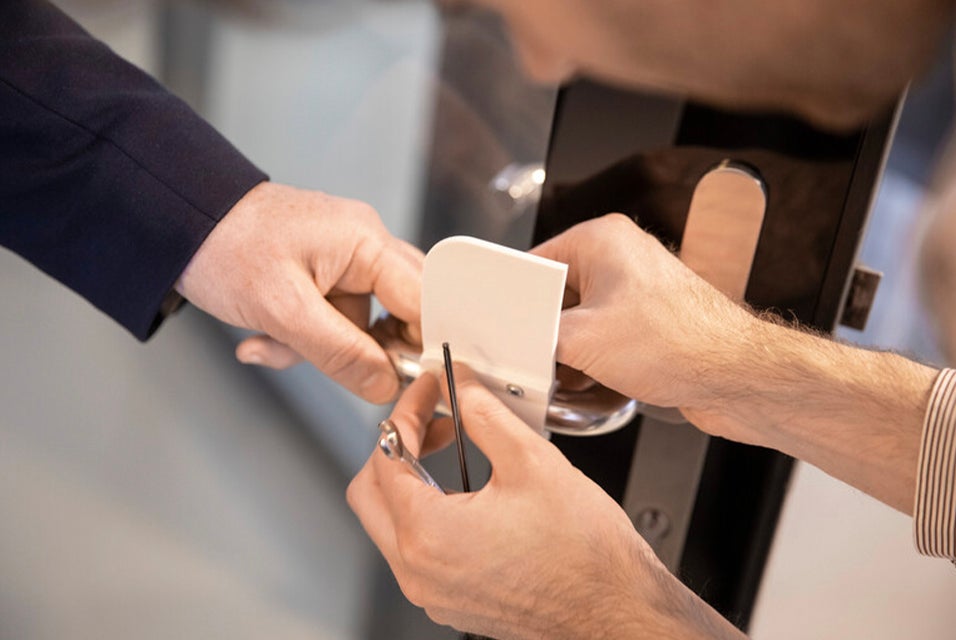 Two people attaching a 3D-printed, hands-free door opener to a door handle