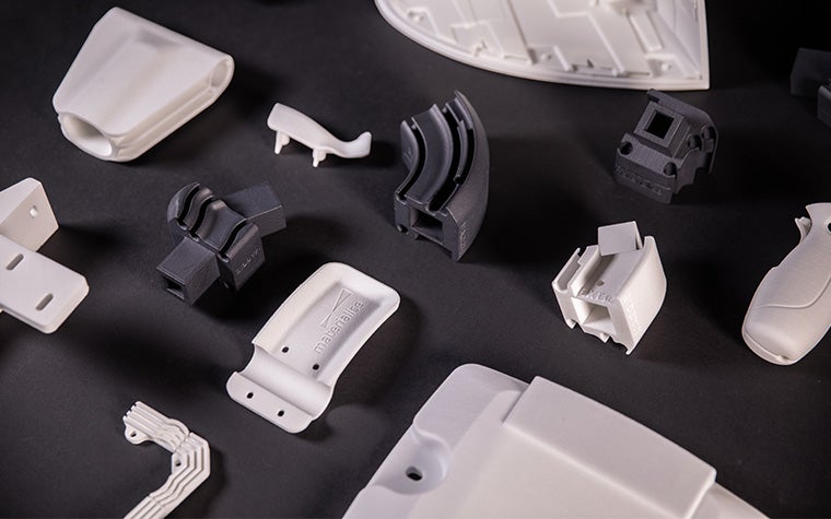 Various black and white 3D-printed parts spread out on a black table, printed with the Bluesint PA 12 technology
