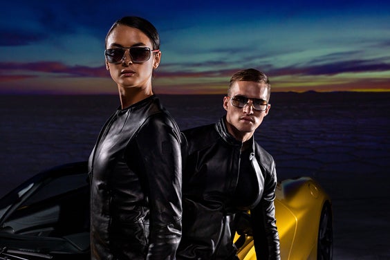 Two models in front of a McLaren sports car wearing 3D-printed sunglasses from the McClaren Vision Collection