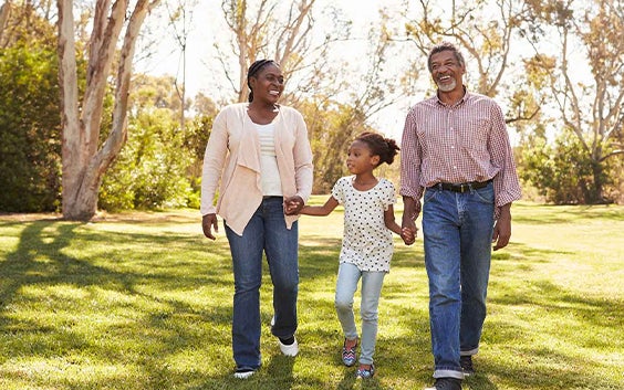 A family of a woman, man, and little girl holding hands and walking through the grass