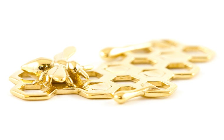 A gold charm in the shape of a honeybee and honeycomb made with lost-wax casting.