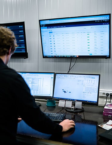 スタンディングデスクで2つのコンピュータスクリーンに向かっている男性。Materialise Nesterモジュールを使用している。