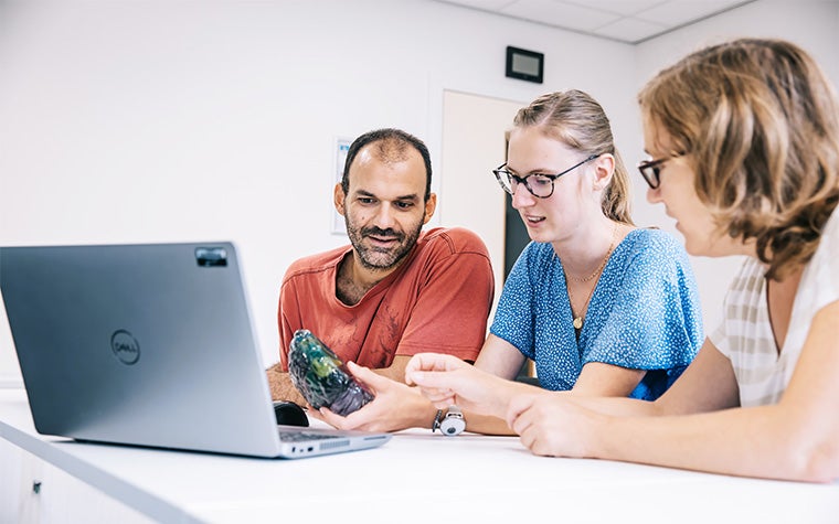 A group of three people sitting at a table, looking at a 3D-printed anatomical model in front of a laptop