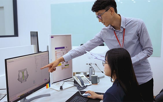 Man pointing to a computer with medical software while speaking to a woman sitting at a desk