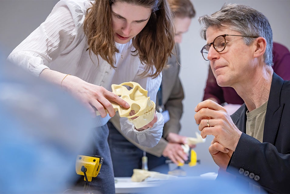 Two colleagues examining a skull model during a hands-on Materialise Dry Bone training session, with surgical tools on a table and other participants visible in the background.