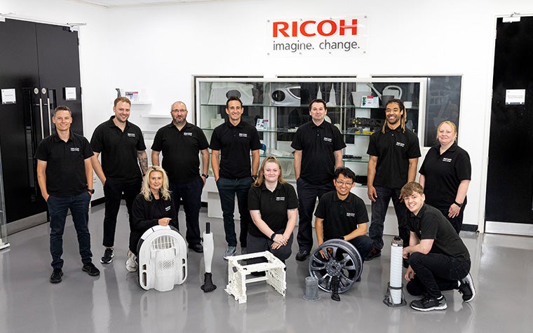 The Ricoh 3D team posts in their office space with various 3D-printed sample pieces