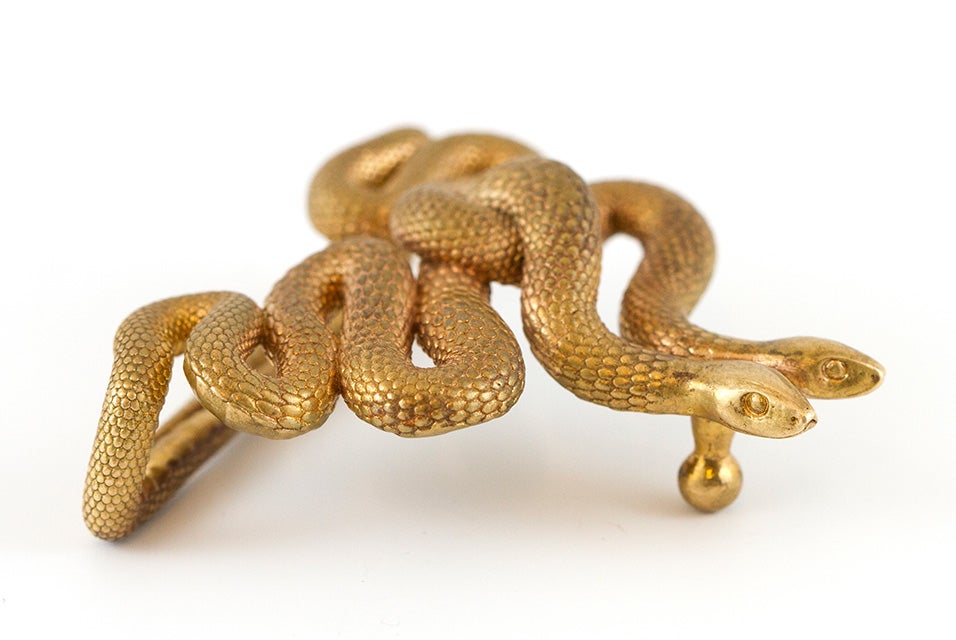 A gold belt buckle in the shape of two intertwining snakes made with lost-wax casting. 