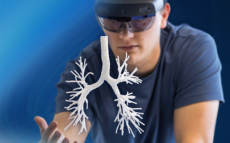Man wearing augmented reality lens while sticking his hand out under a 3D-printed model of lung anatomy. The blue Mimics swirl is in the background