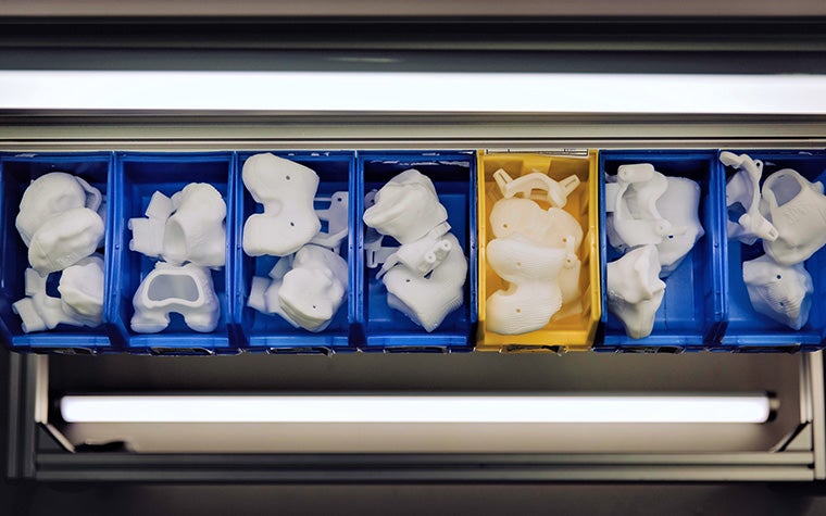 six blue containers and one orange container filled with personalized 3D-printed surgical implants