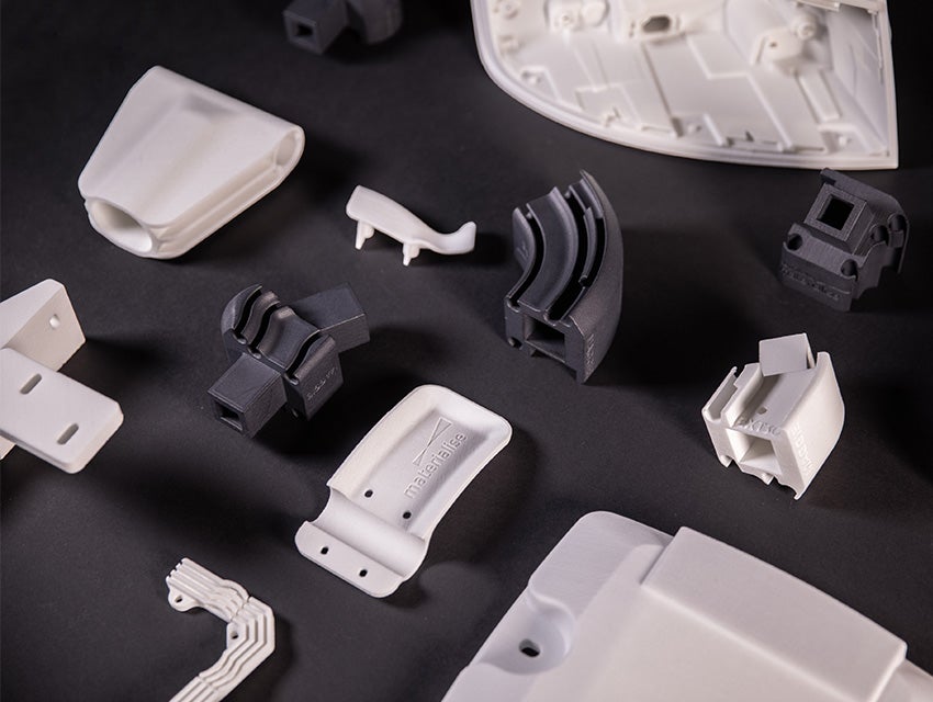 Various black and white 3D-printed parts spread out on a black table, printed with the Bluesint PA 12 technology
