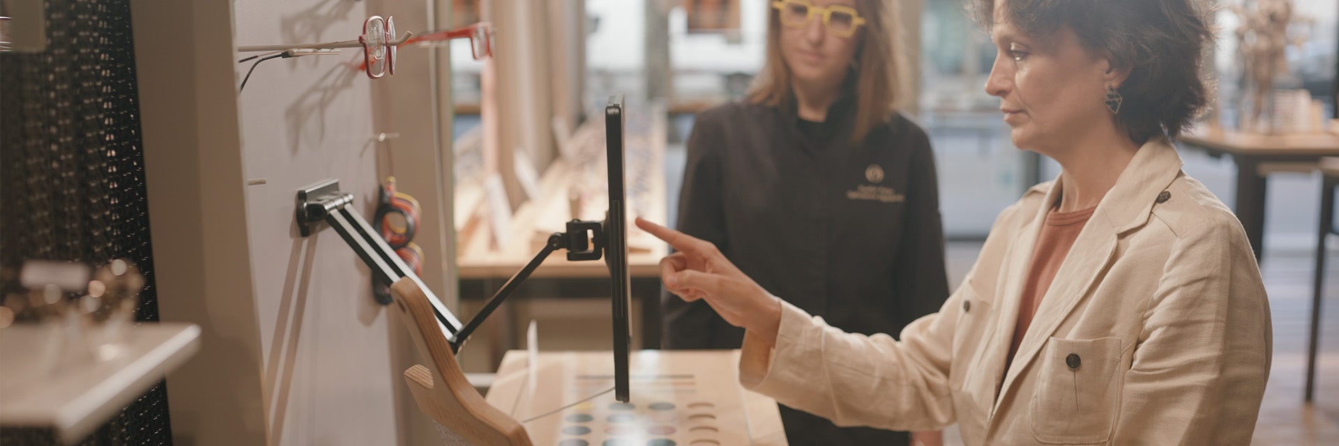 Una donna utilizza la Materialise Eyewear Fitting Suite su un iPad in un negozio Acuitis, osservata dal suo ottico.