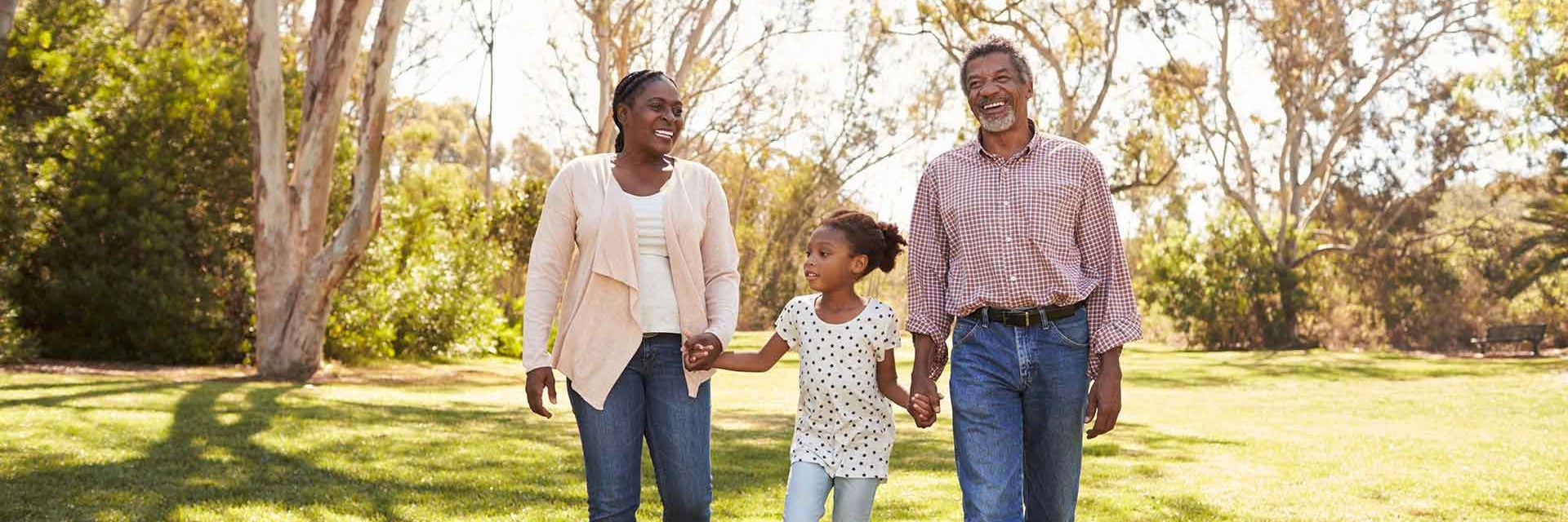 A family of a woman, man, and little girl holding hands and walking through the grass
