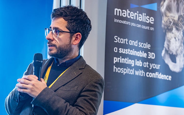 Ferran Fillat-Gomà speaks in front of a printed Materialise banner featuring text about starting and scaling a 3D-printing lab.