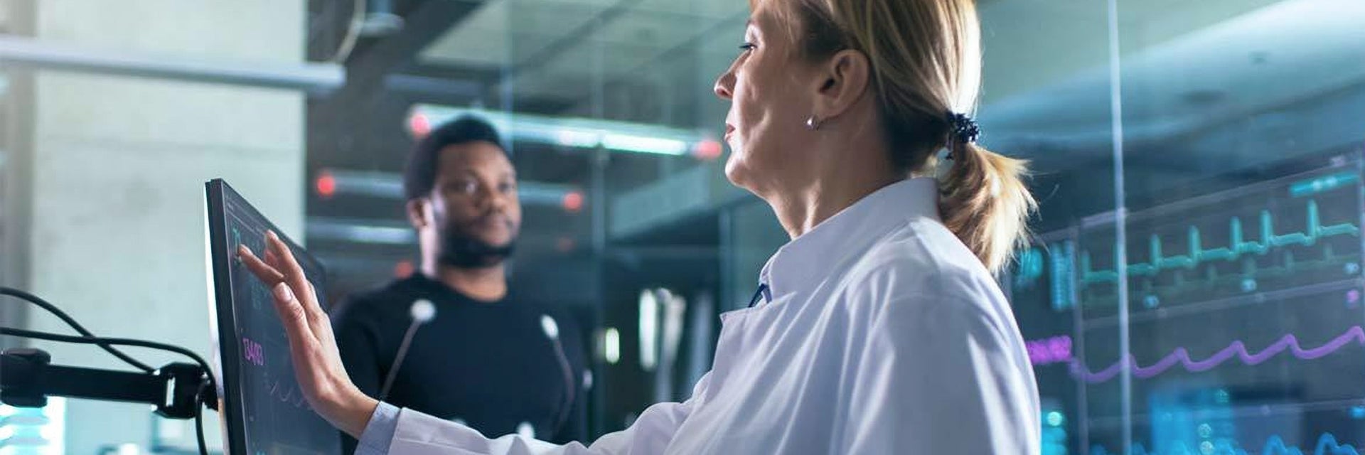 Femme touchant un écran tactile dans un laboratoire de recherche avec un homme derrière elle