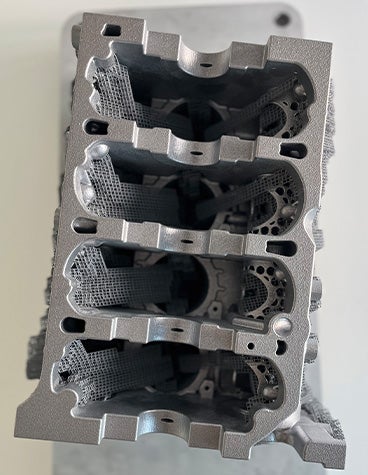 A top-down view of a metal 3D-printed crankcase produced by the BÖLLINGER GROUP sitting on a wooden table.