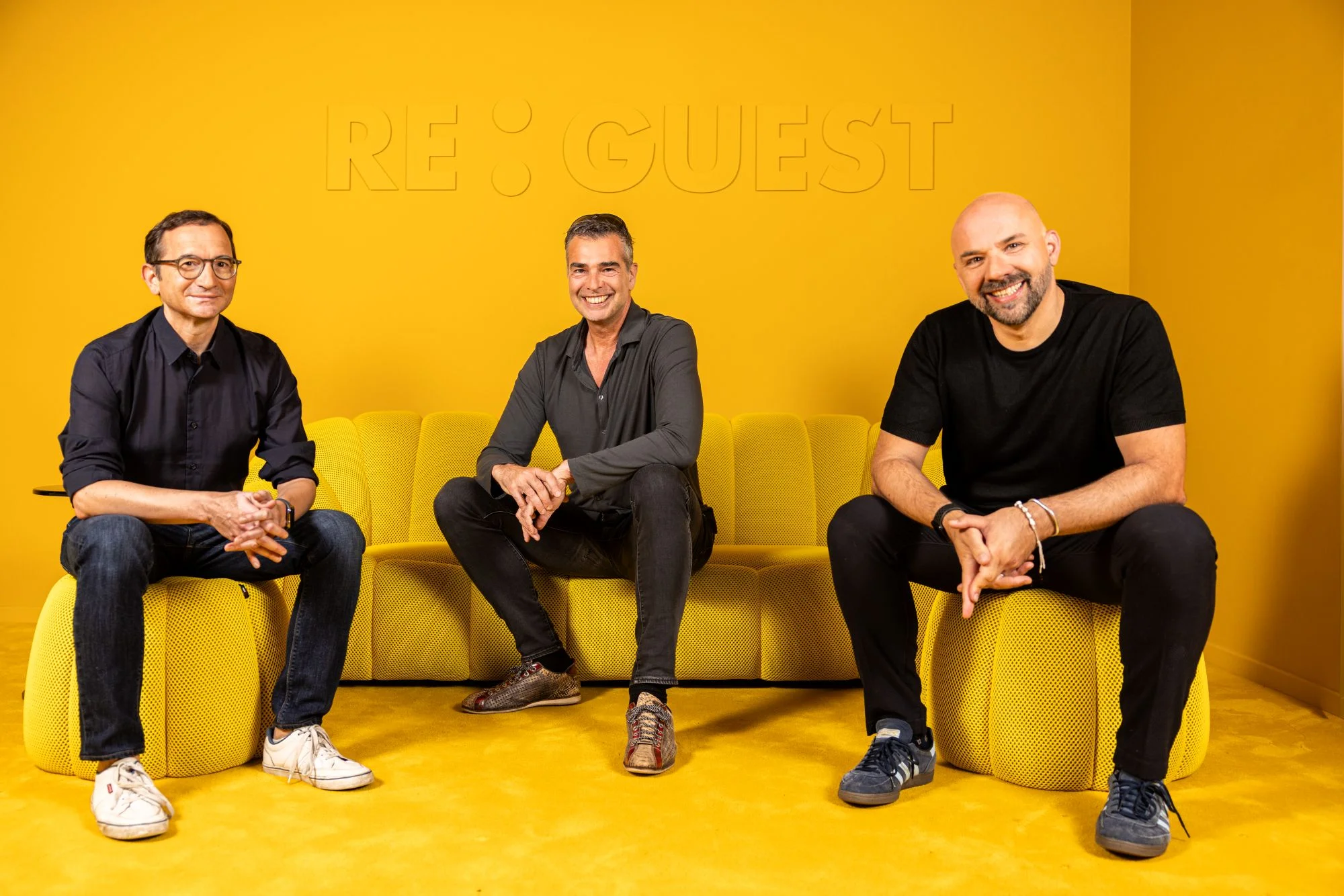 Stefan Plattner, Michael Mitterhofer und Denis Pelligrini von ReGuest sitzen auf einem gelben Sofa vor dem Firmenlogo.