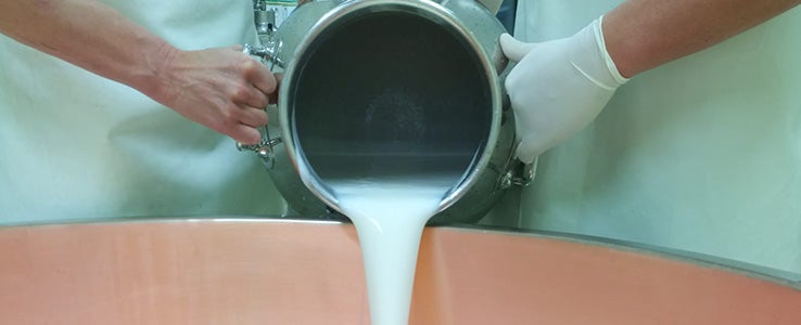 Milch wird in einen Kessel geschüttet