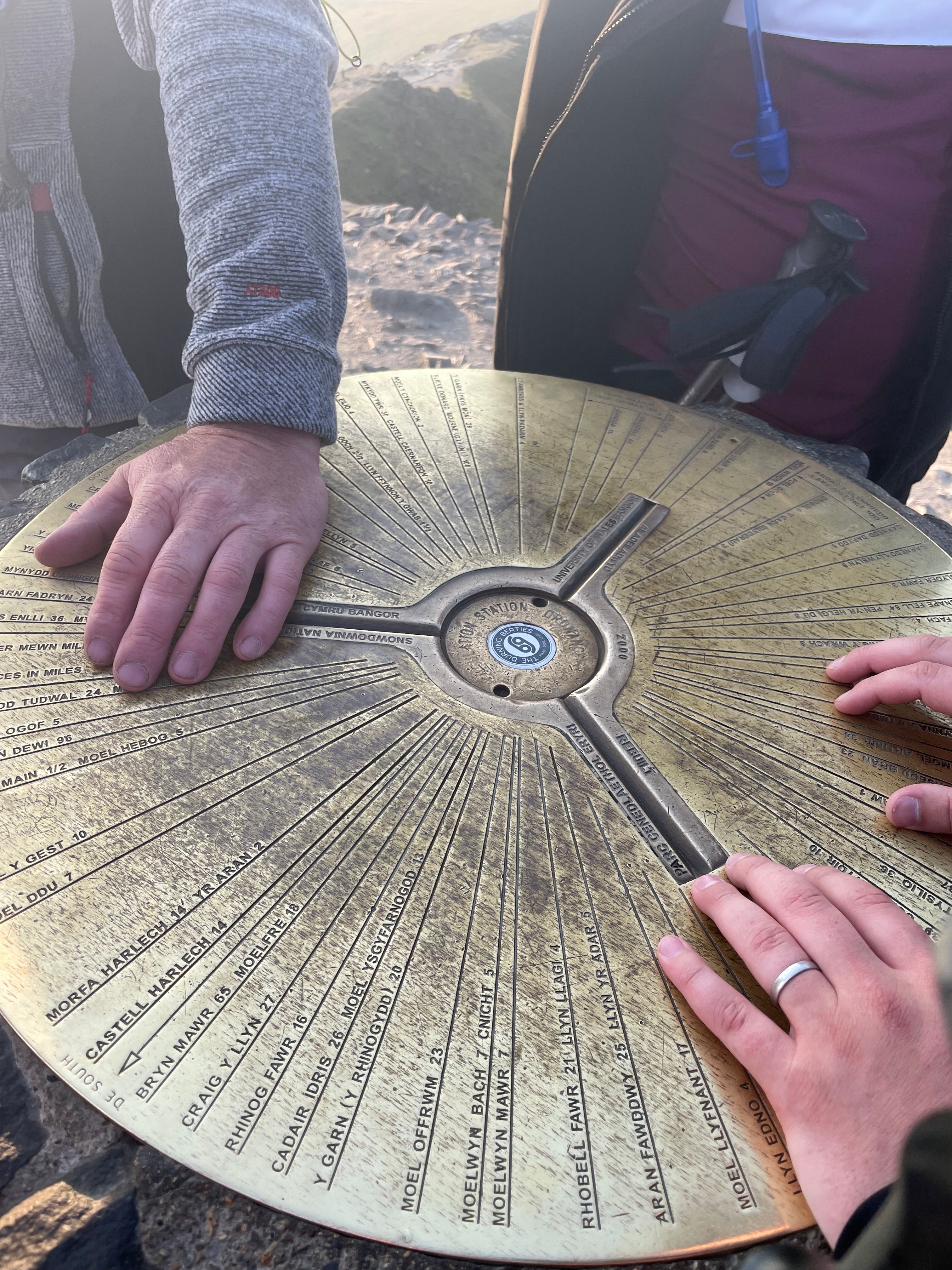 Three hands touching the Yr Wyddfa (Snowdon) summit marker