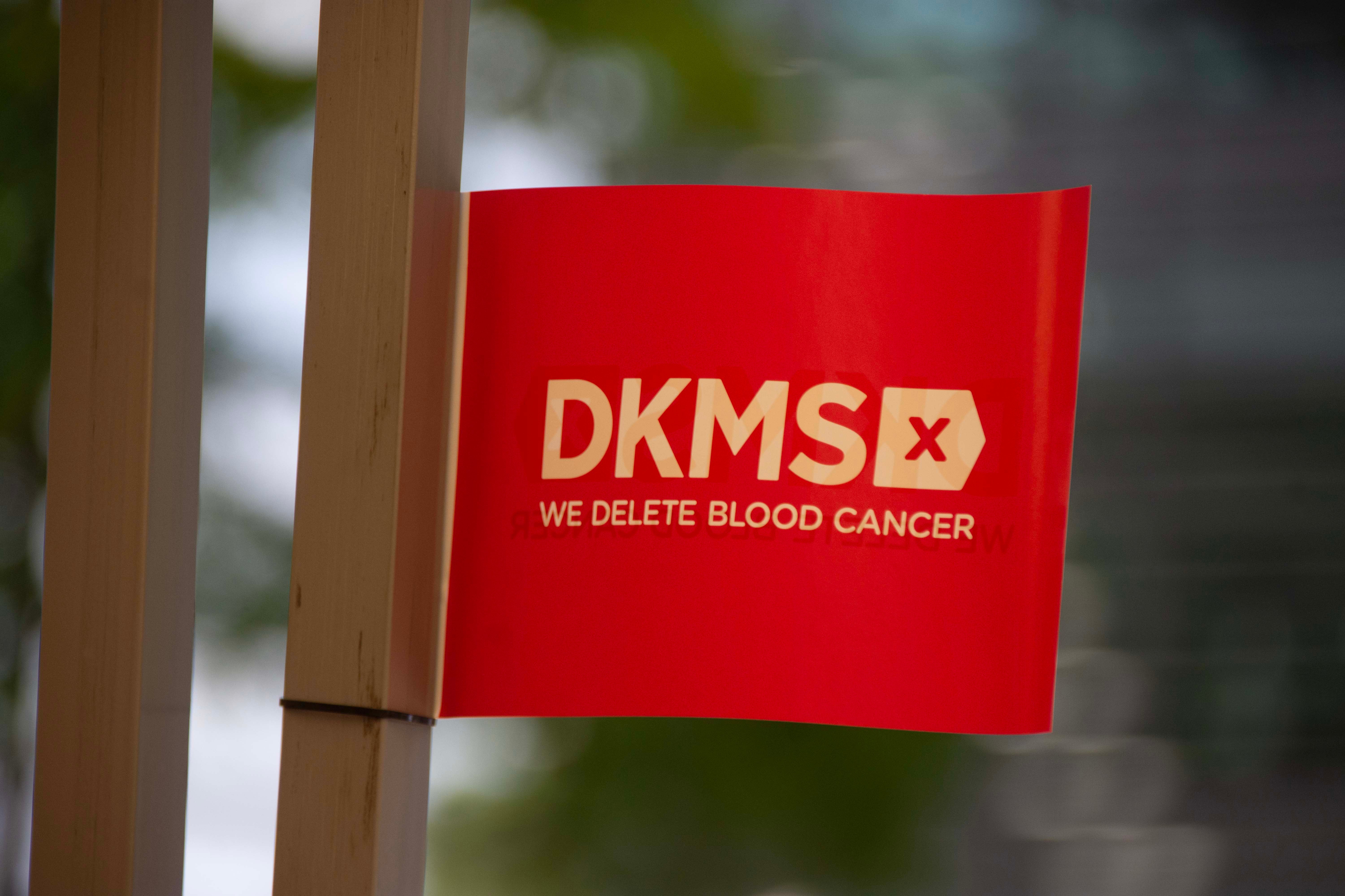 Red flag showing white DKMS logo and tagline 'We delete blood cancer'