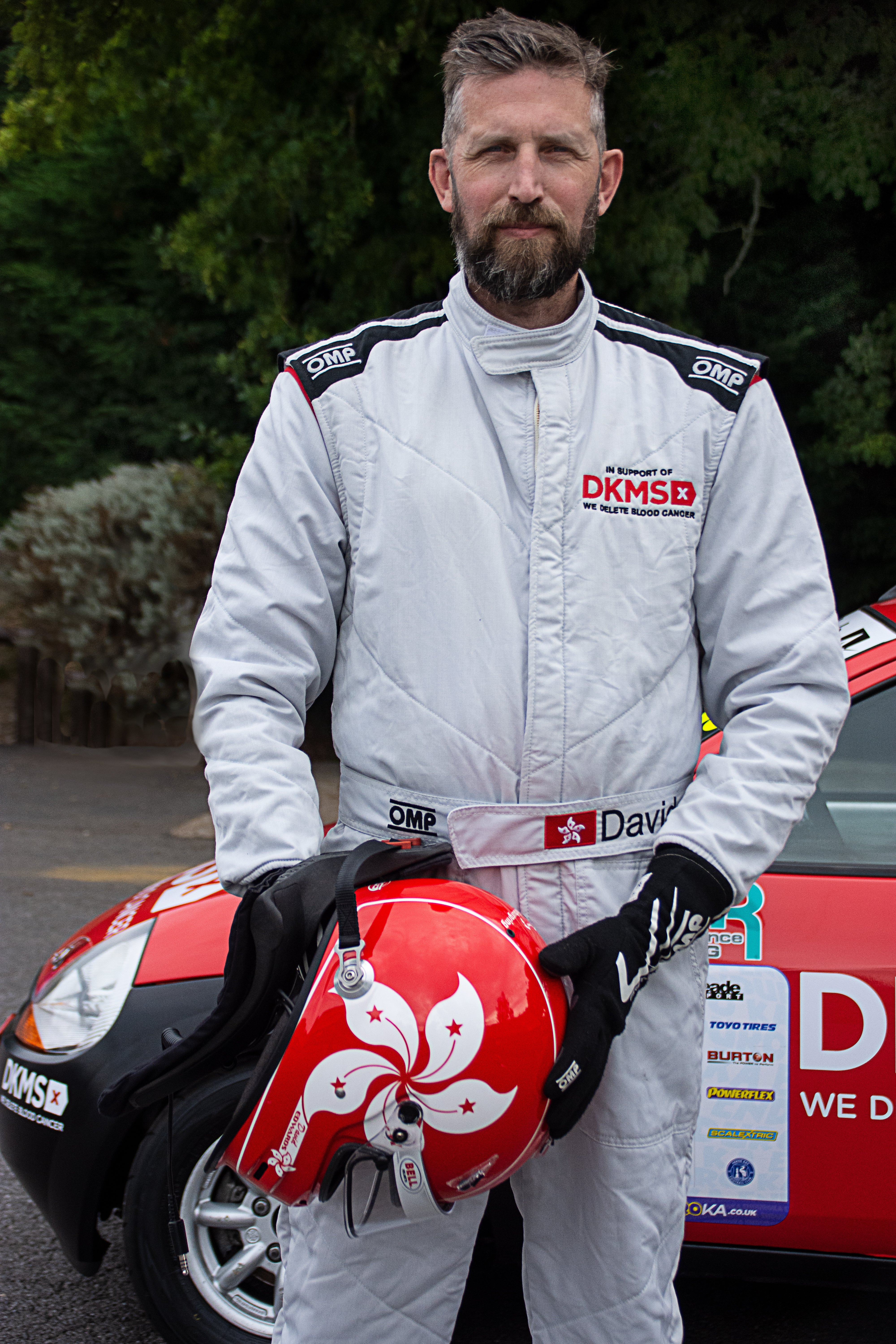 David Edwards wearing DKMS racing suit and holding a red helmet