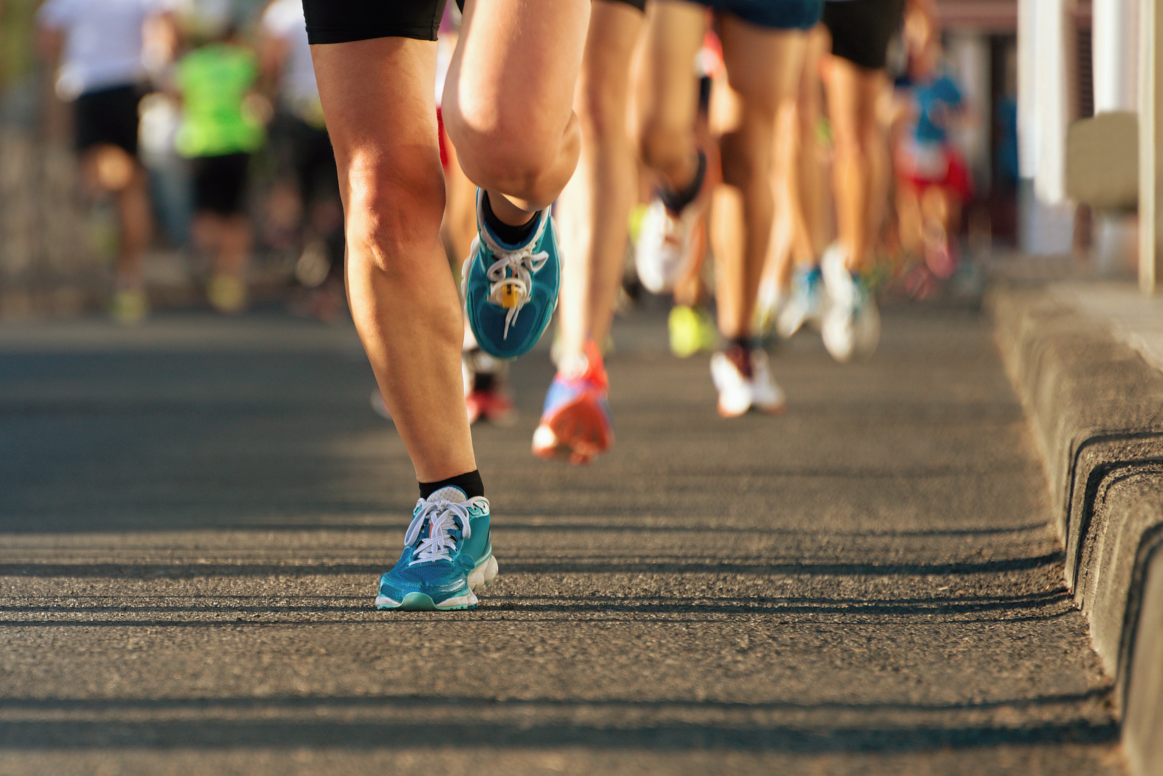 Legs of runners in a race, running on asphalt.