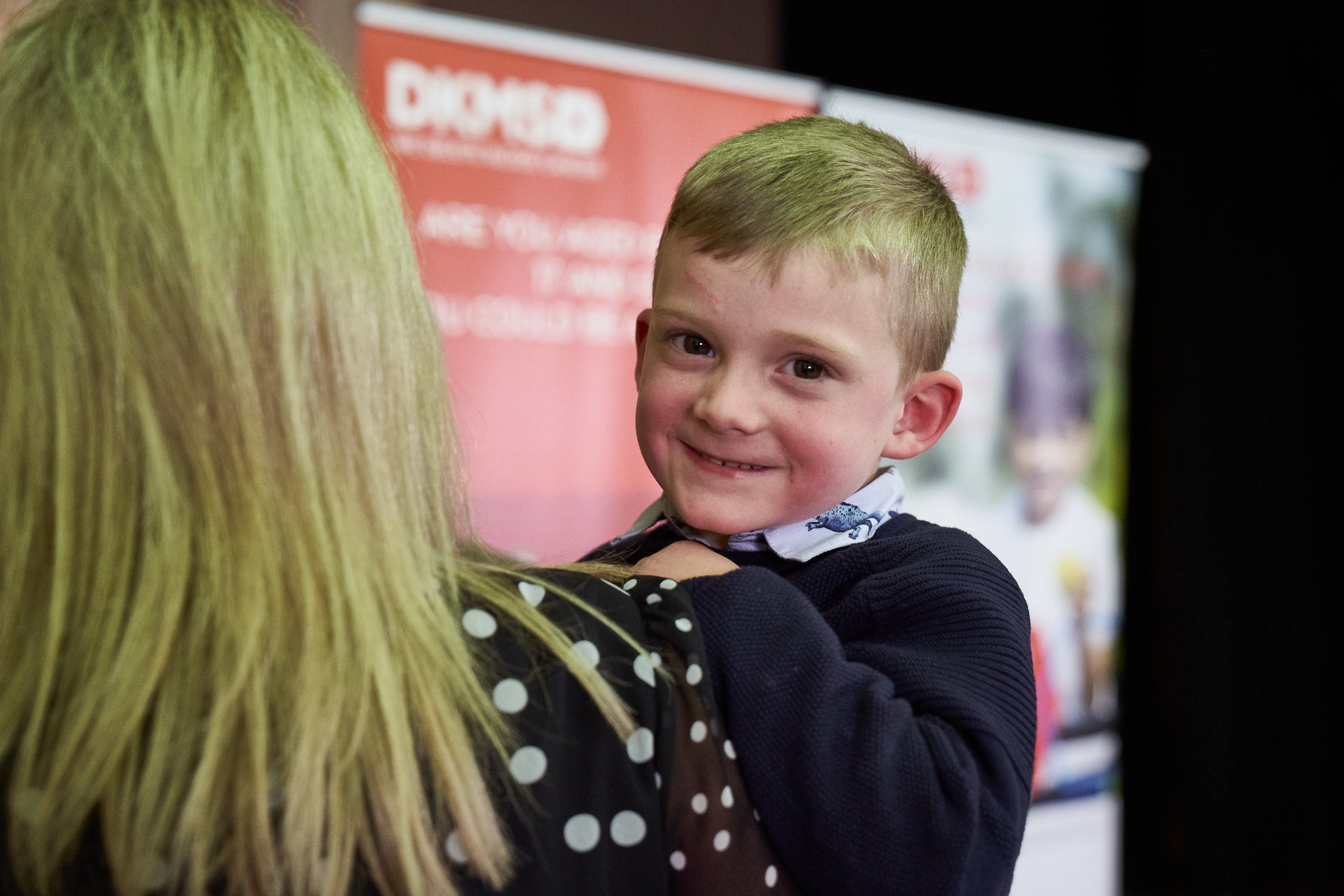 Alfie being held by his Mum, smiling into the camera. 