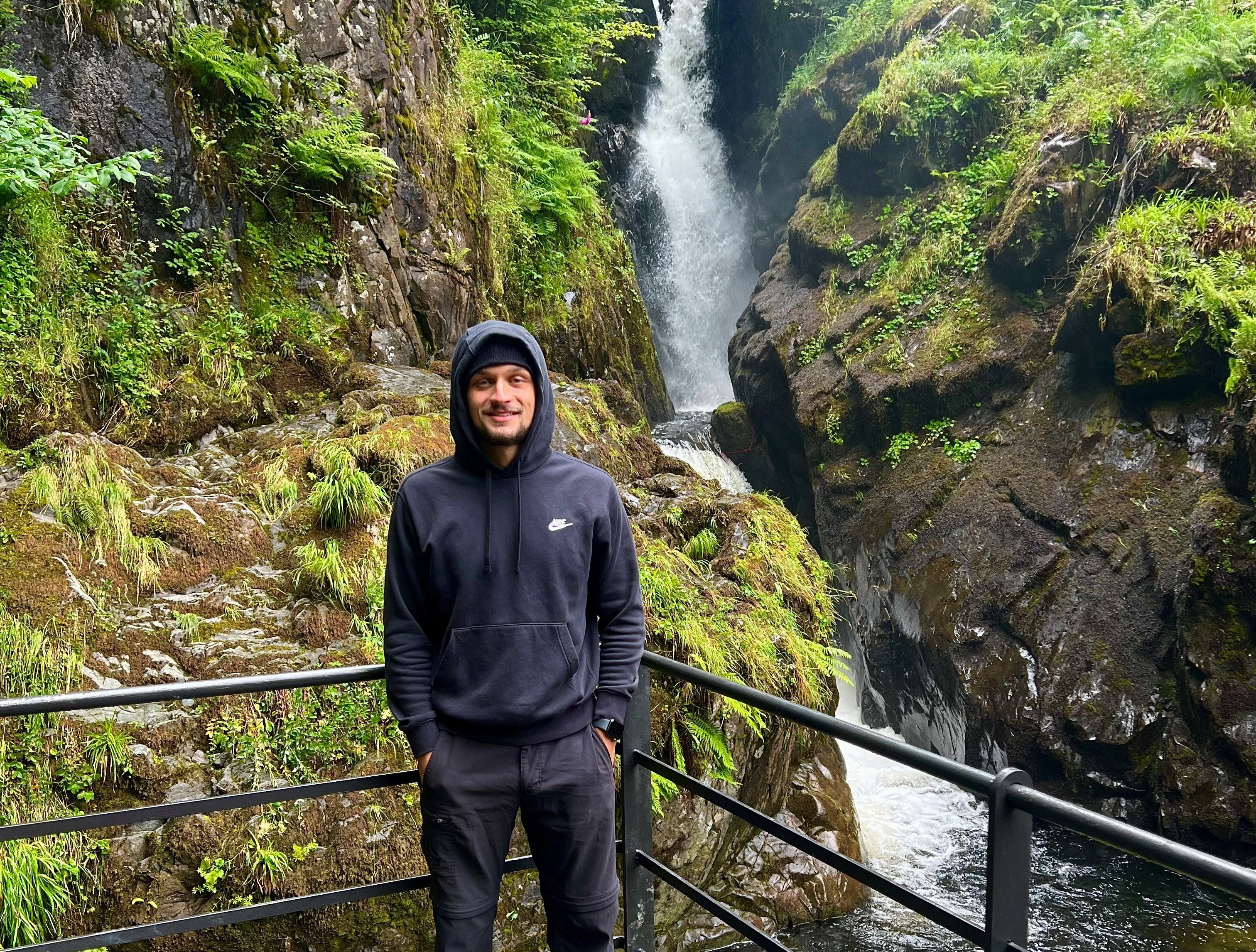 Man in a sweatshirt standing in front of a waterfall