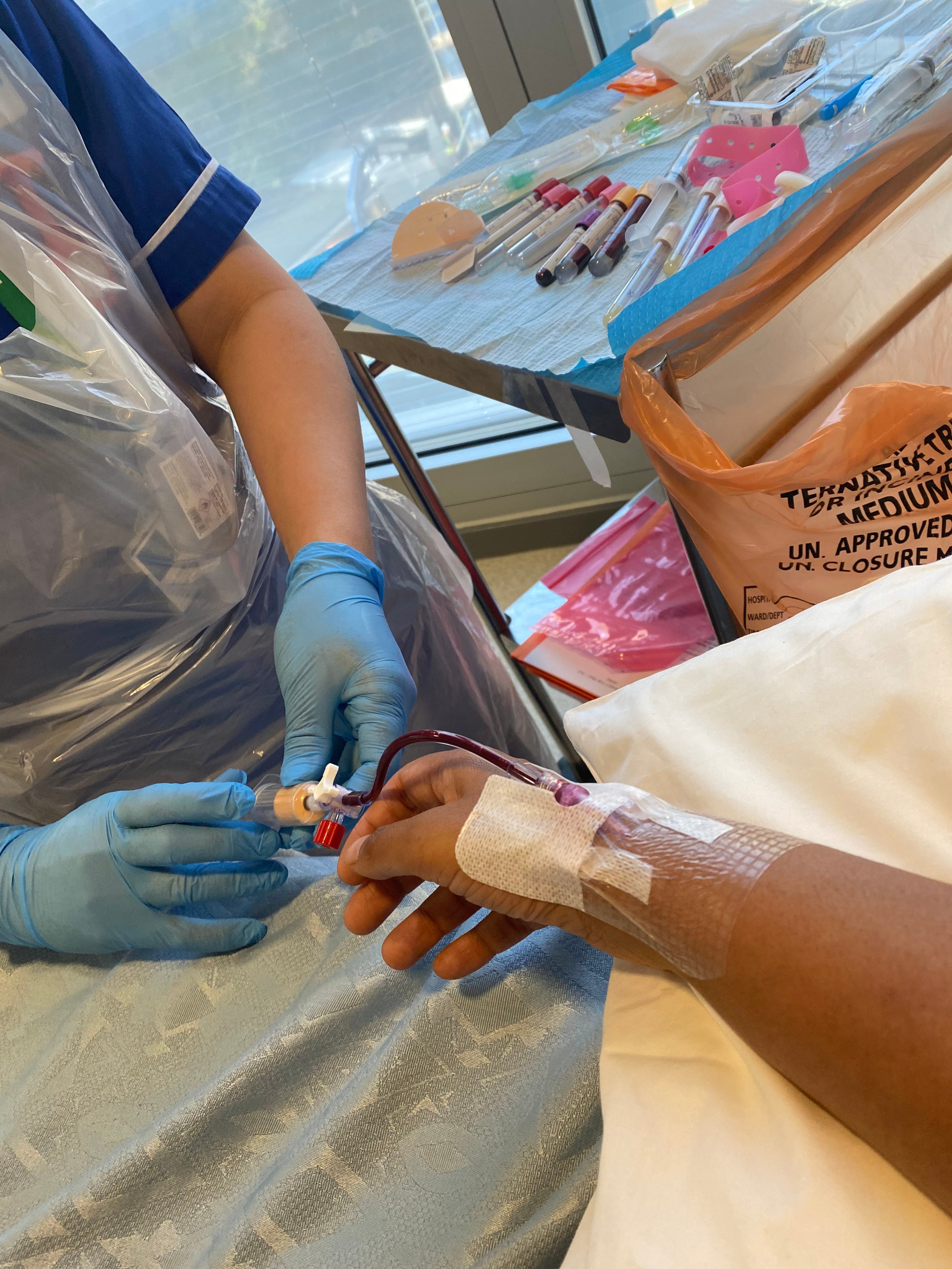 A nurse inserting a cannula into Poonam's arm to extract her blood through to the apherisis machine. 