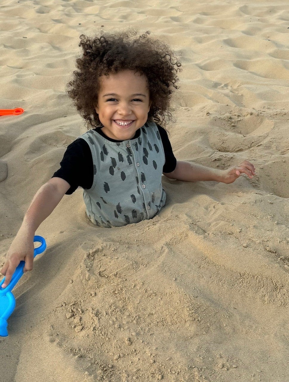 Little boy in the sand smiling at the beach