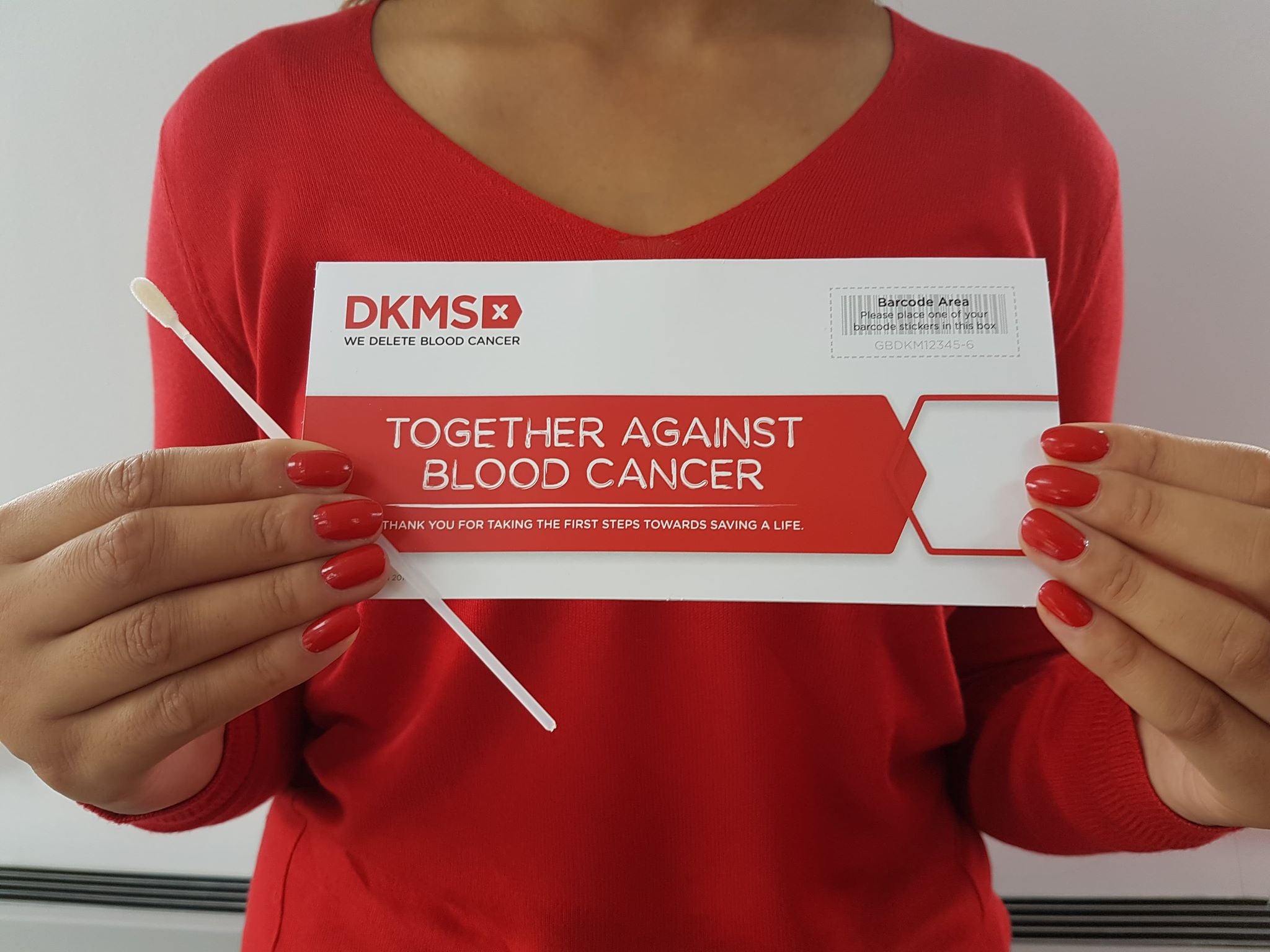 Woman dressed in DKMS red holding swab kit with Freepost envelope