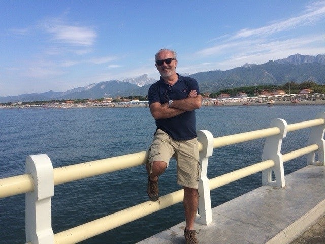 Elderly white man smiling and leaning on a railing