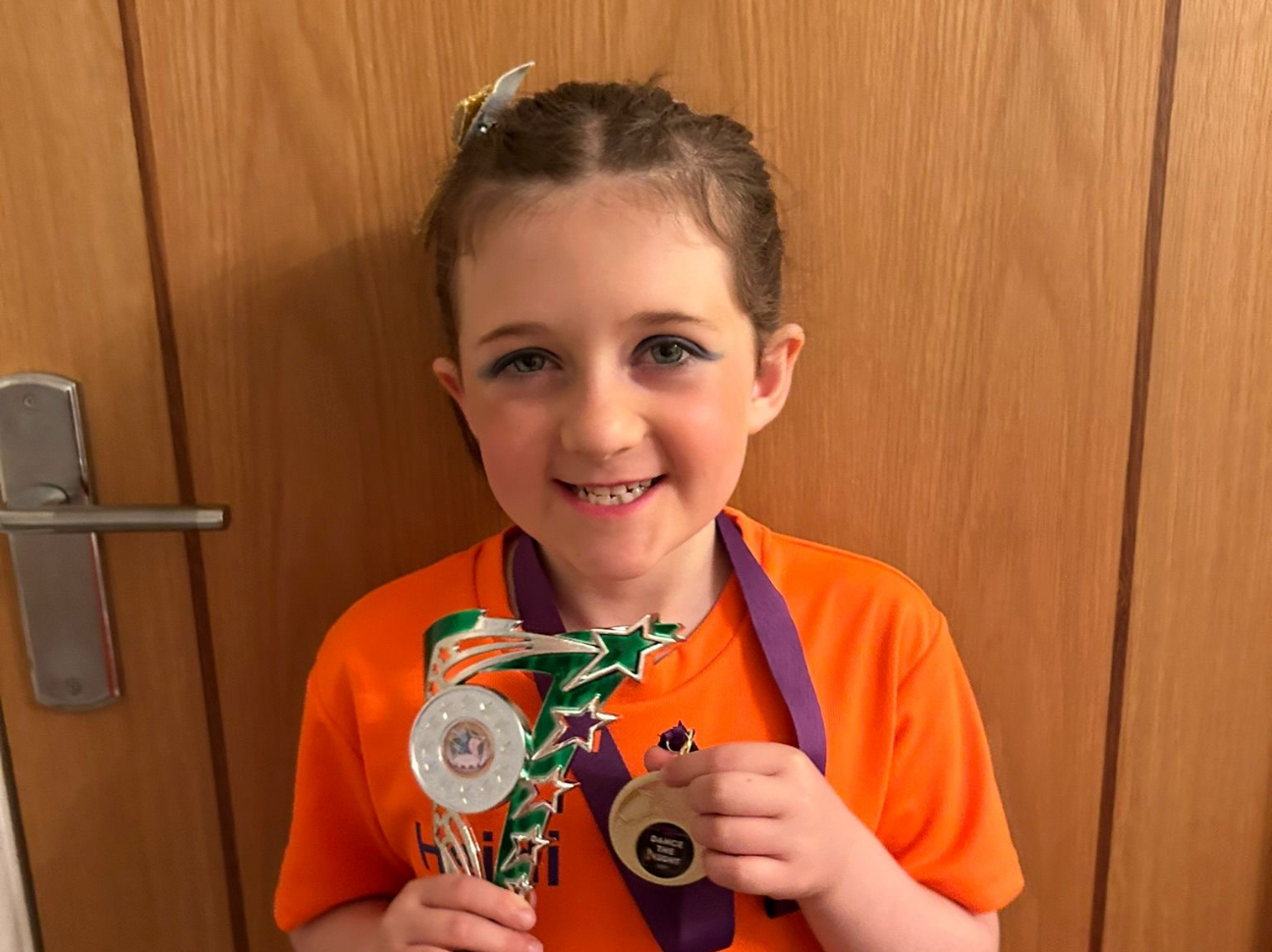 Little girl smiles while holding a trophy and a medal. 