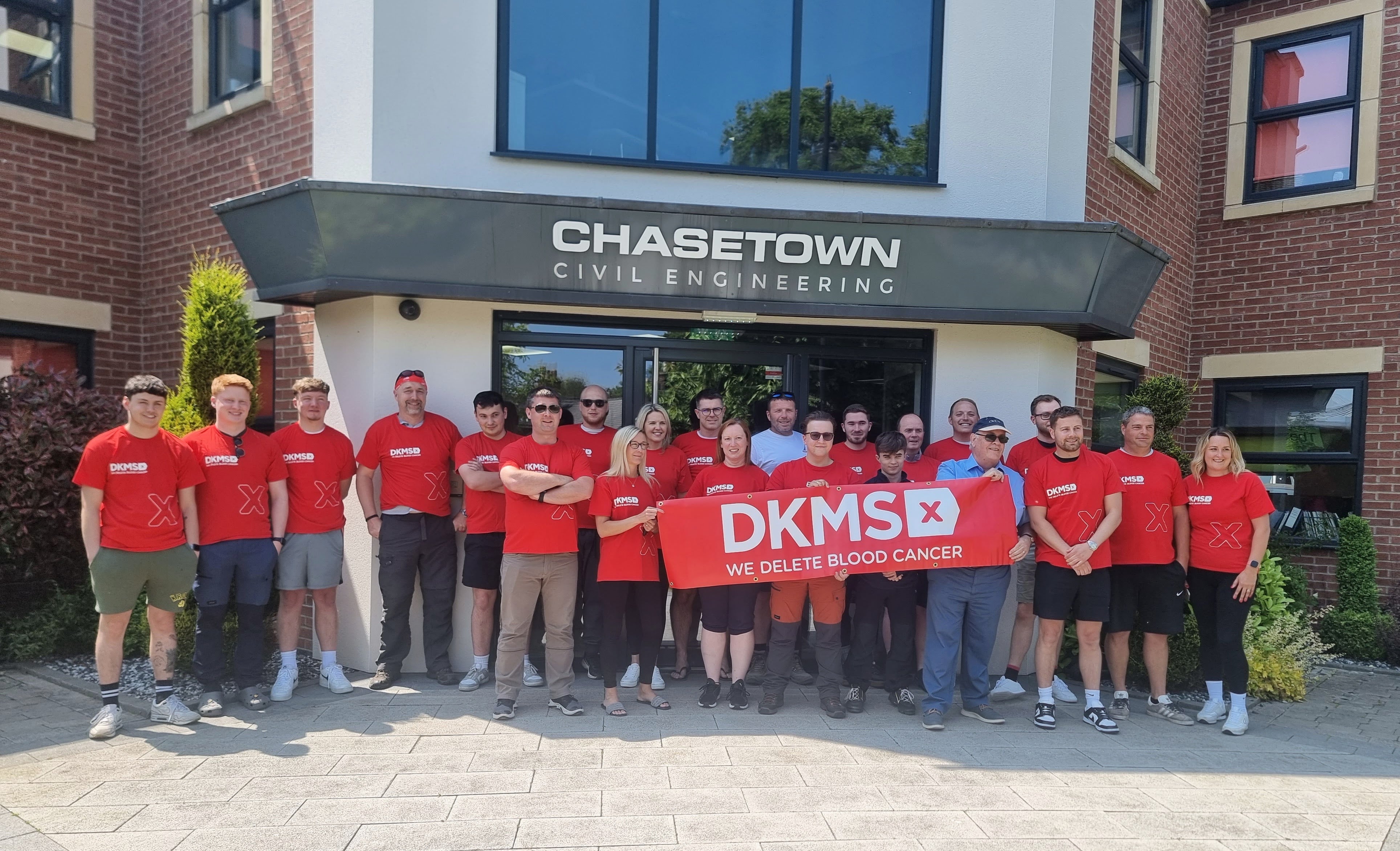 Chasetown Civil Engineering staff outside ther offices wearing DKMS T-shirts and holding a DKMS banner