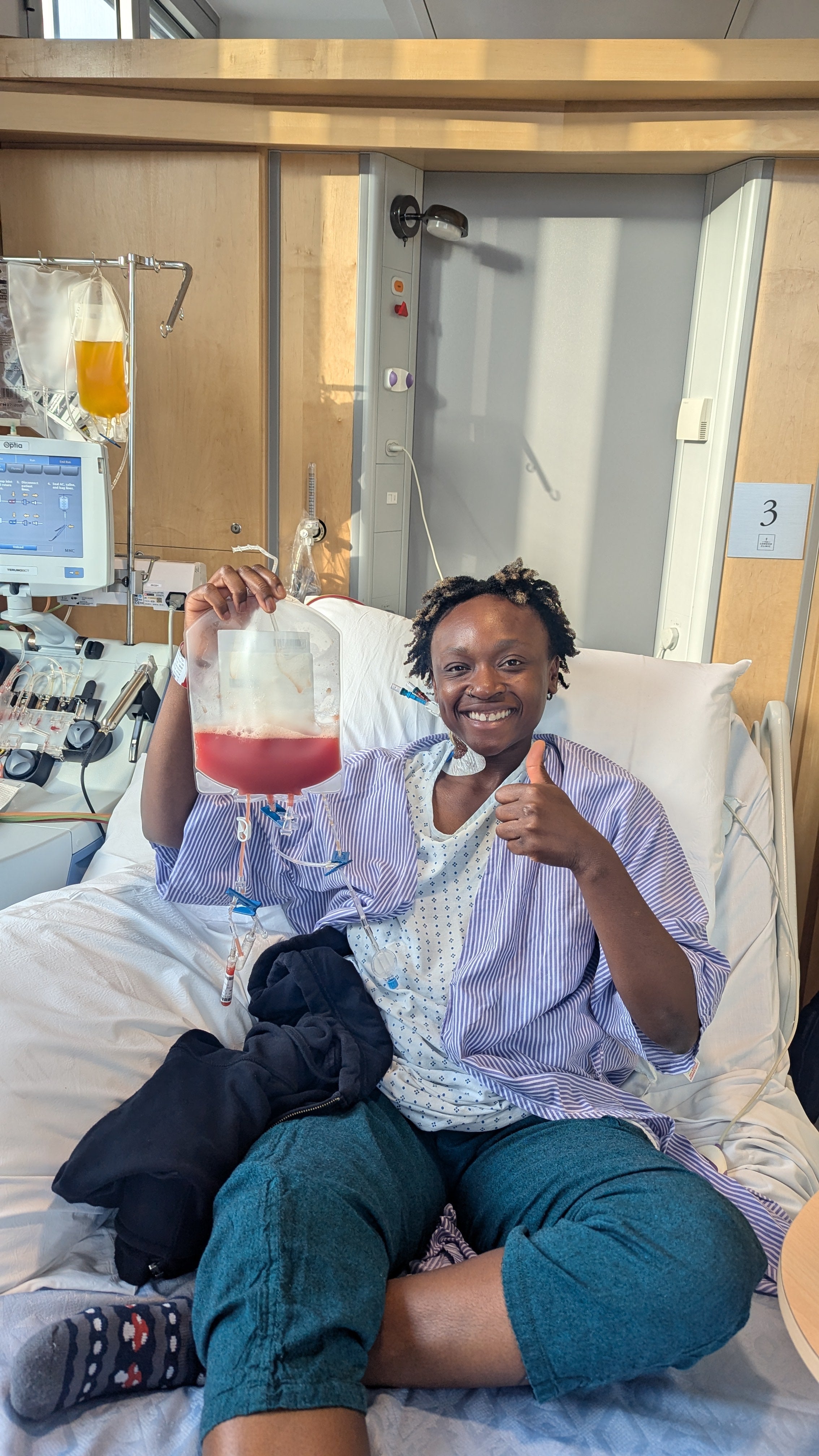 Black woman holding a bag of stem stells in a hospital bed and smiling