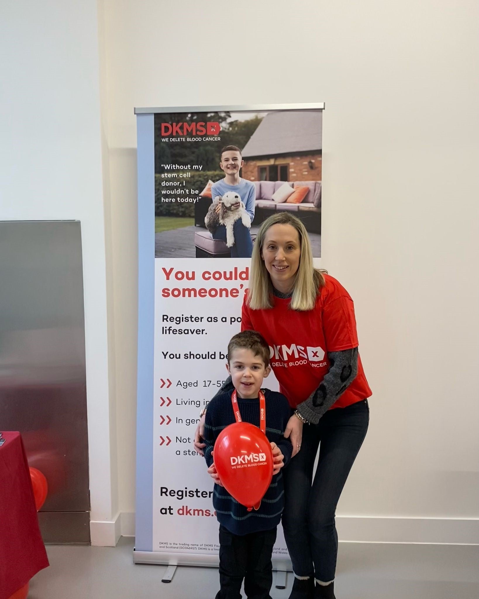 Middle aged white woman wearing a DKMS branded t-shirt holding her son