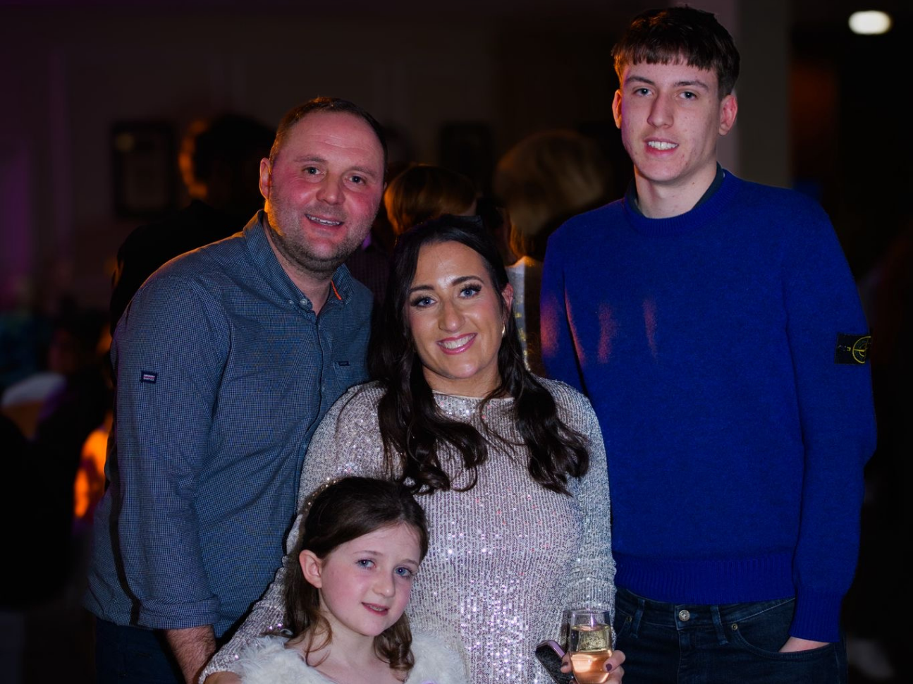 A mum, dad, big brother and little sister pose together and smile at an event. 