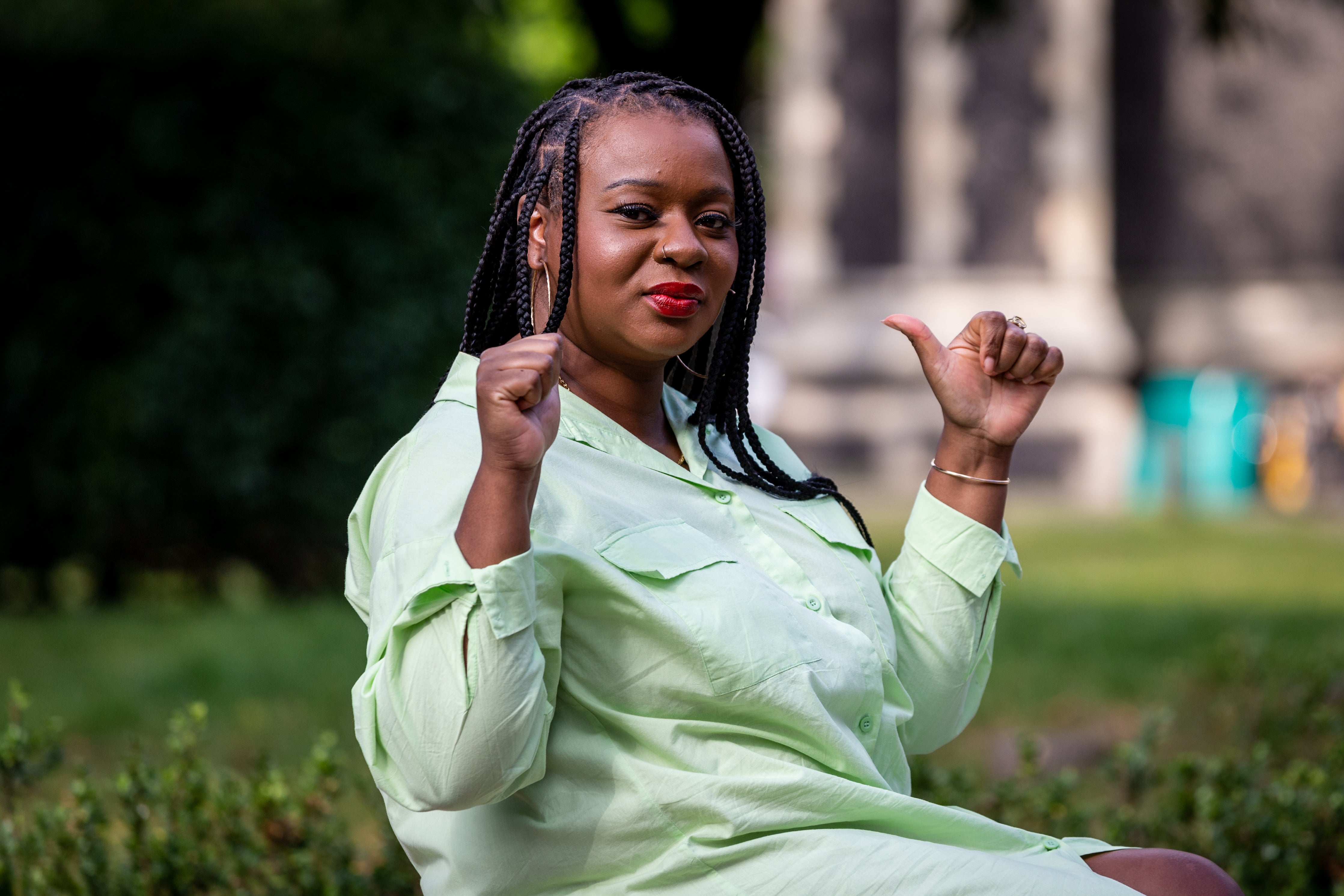 Image of a black woman  with her thumbs up sitting in a park