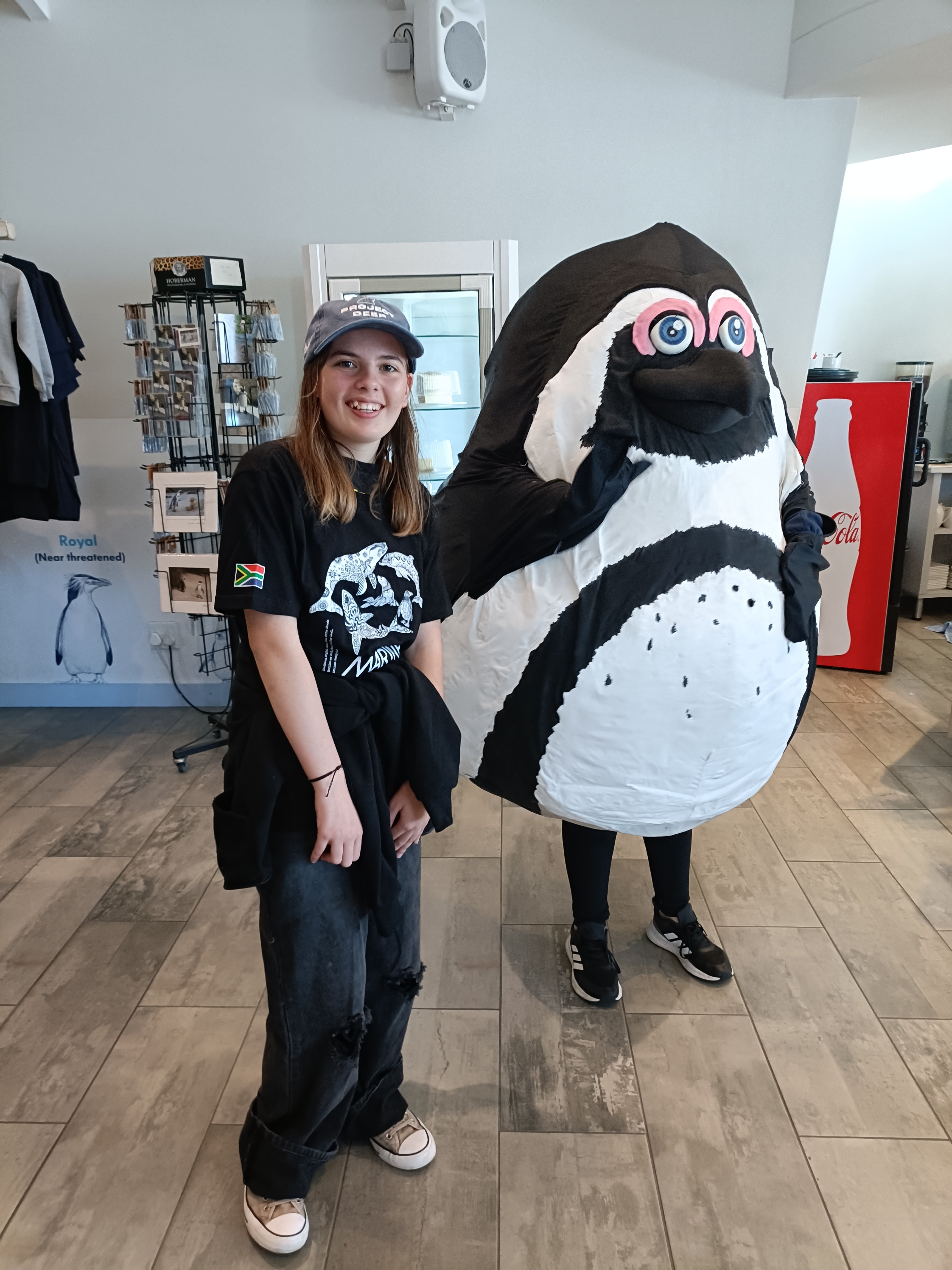 Alba wearing a graphic tee stood next to a penguin character 