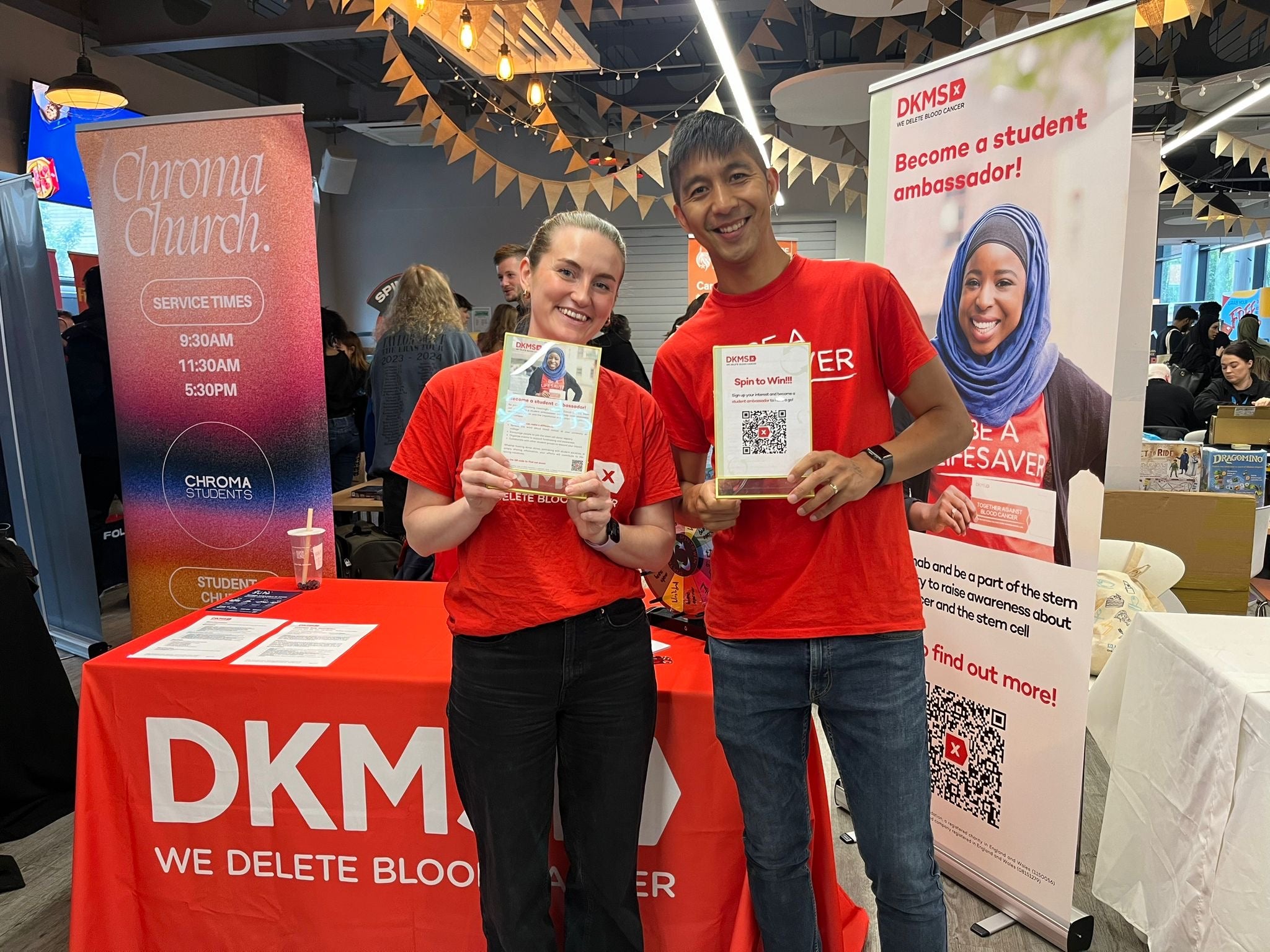 Young Asian man and young white woman holding DKMS branded material at an event.
