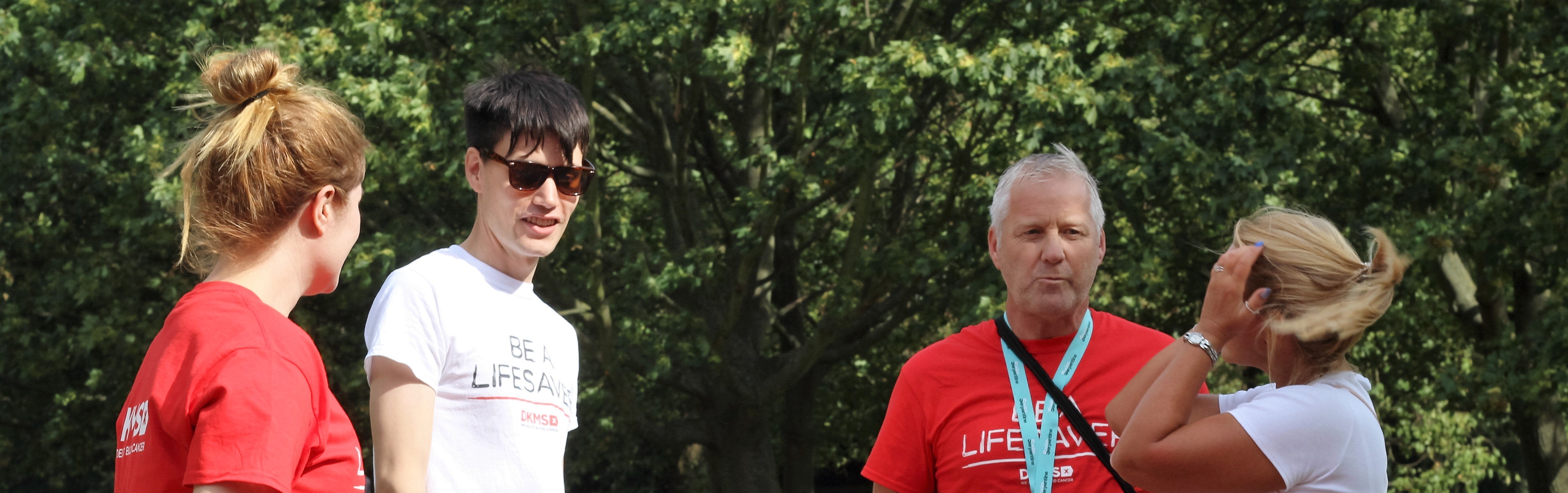 Four people wearing DKMS t-shirts chatting