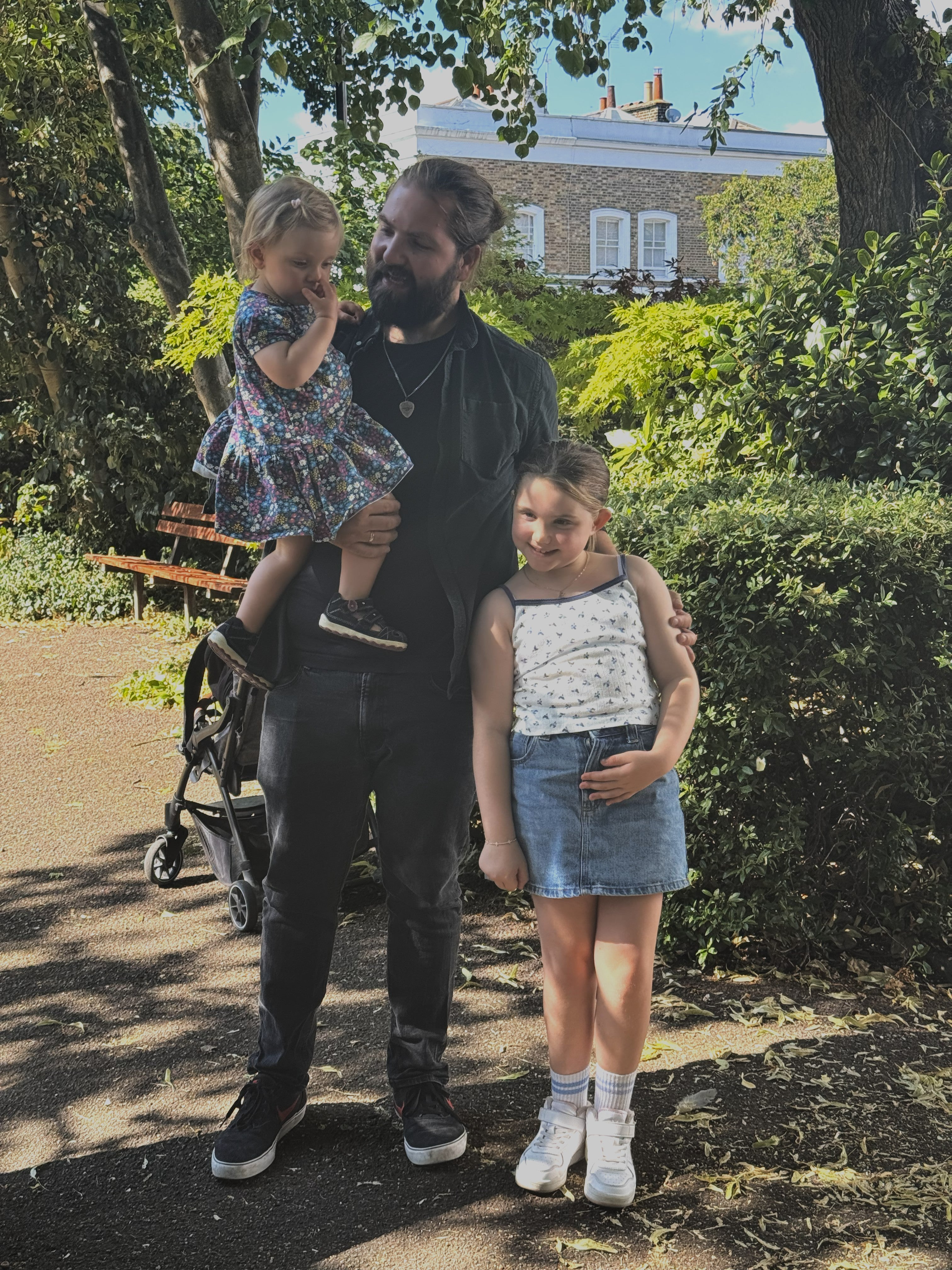 8 year old patient, Emilia, stands in a park in the sun with Jan, the man who saved her life through stem cell donation, and his daughter Emma