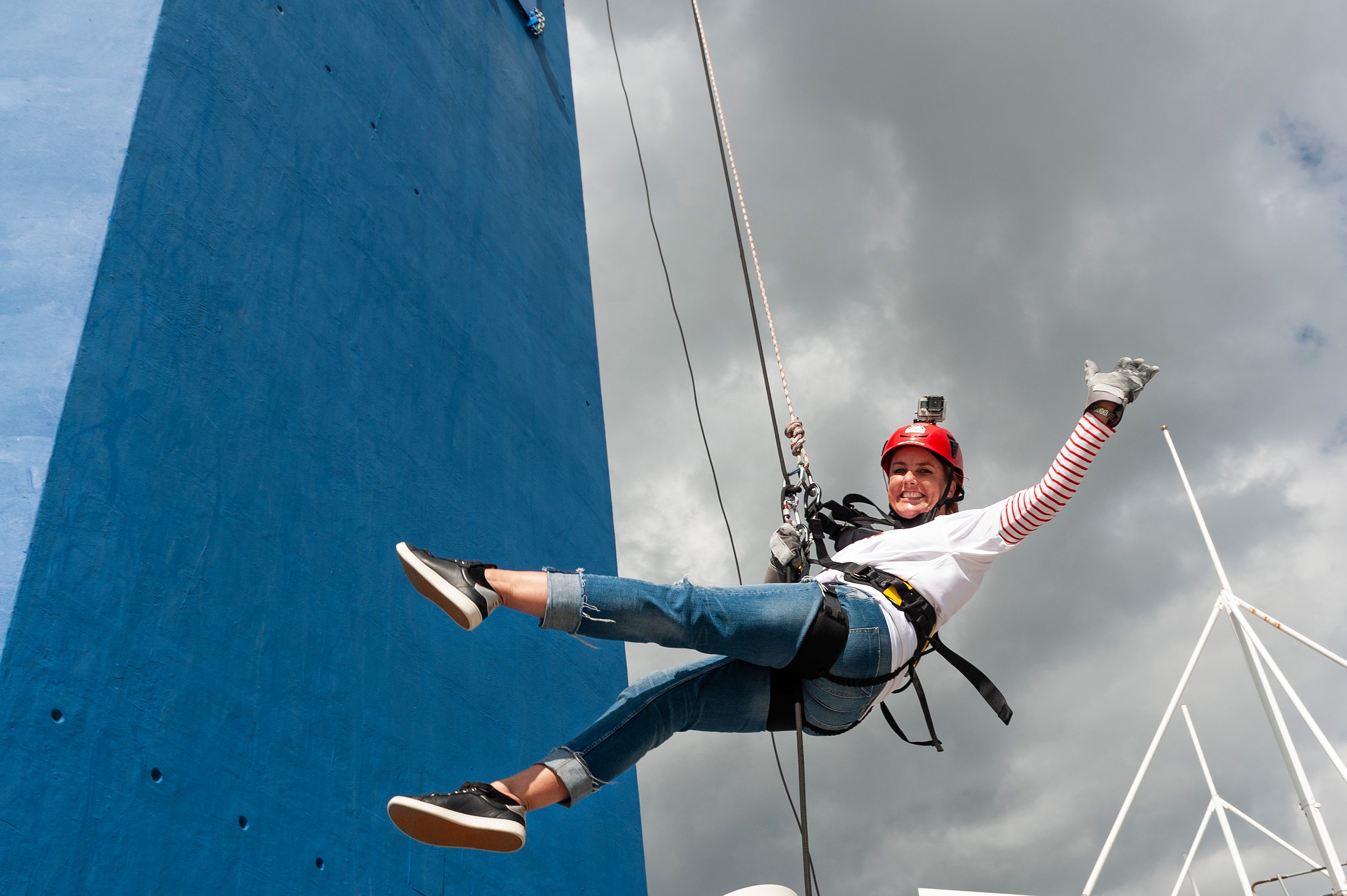 Sally on a harness waving to the camera as she abseils the Spinnaker Tower. 