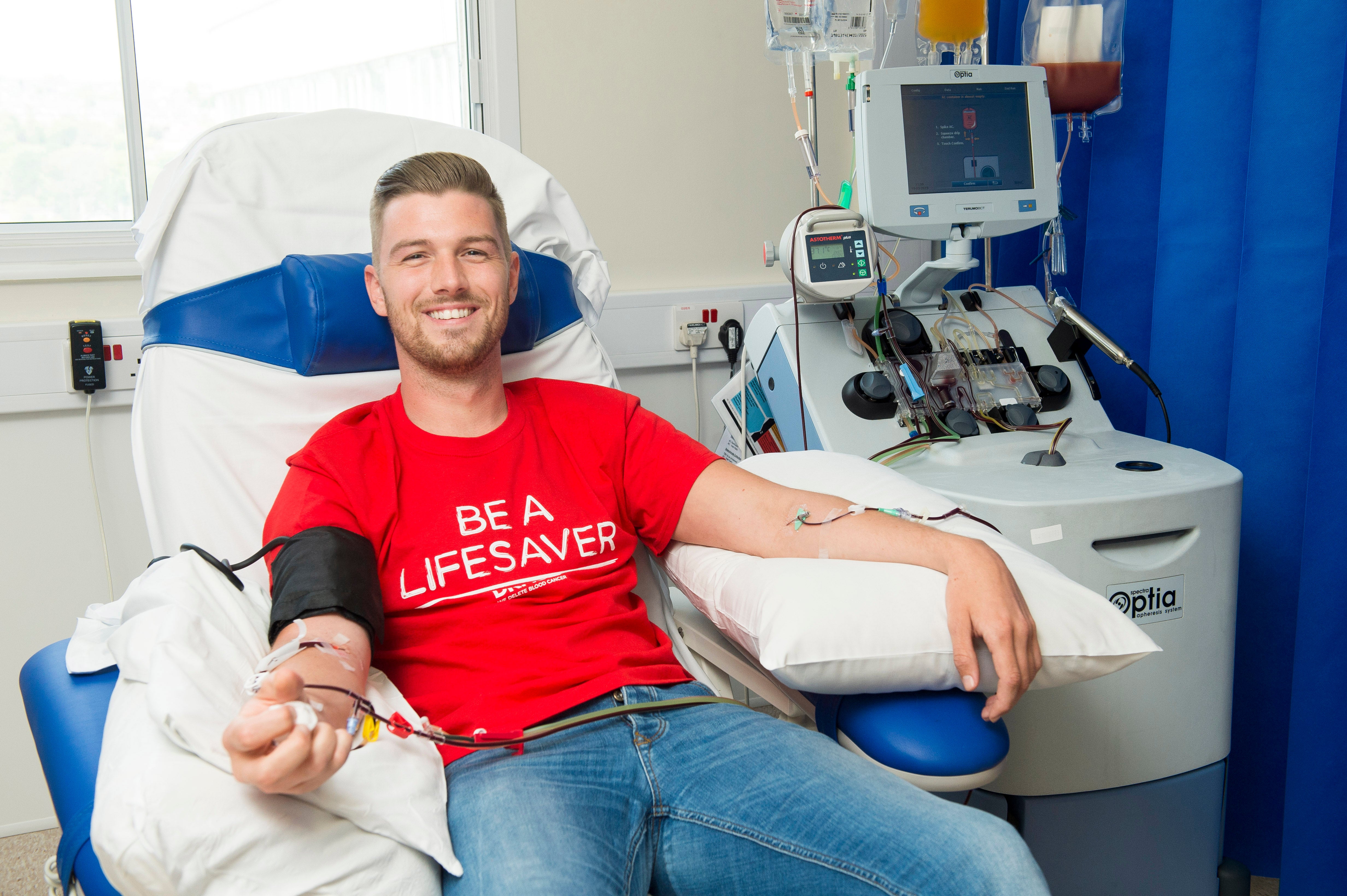 Person in a hospital chair, wearing a DKMS t-shirt, donating blood stem cells. 
