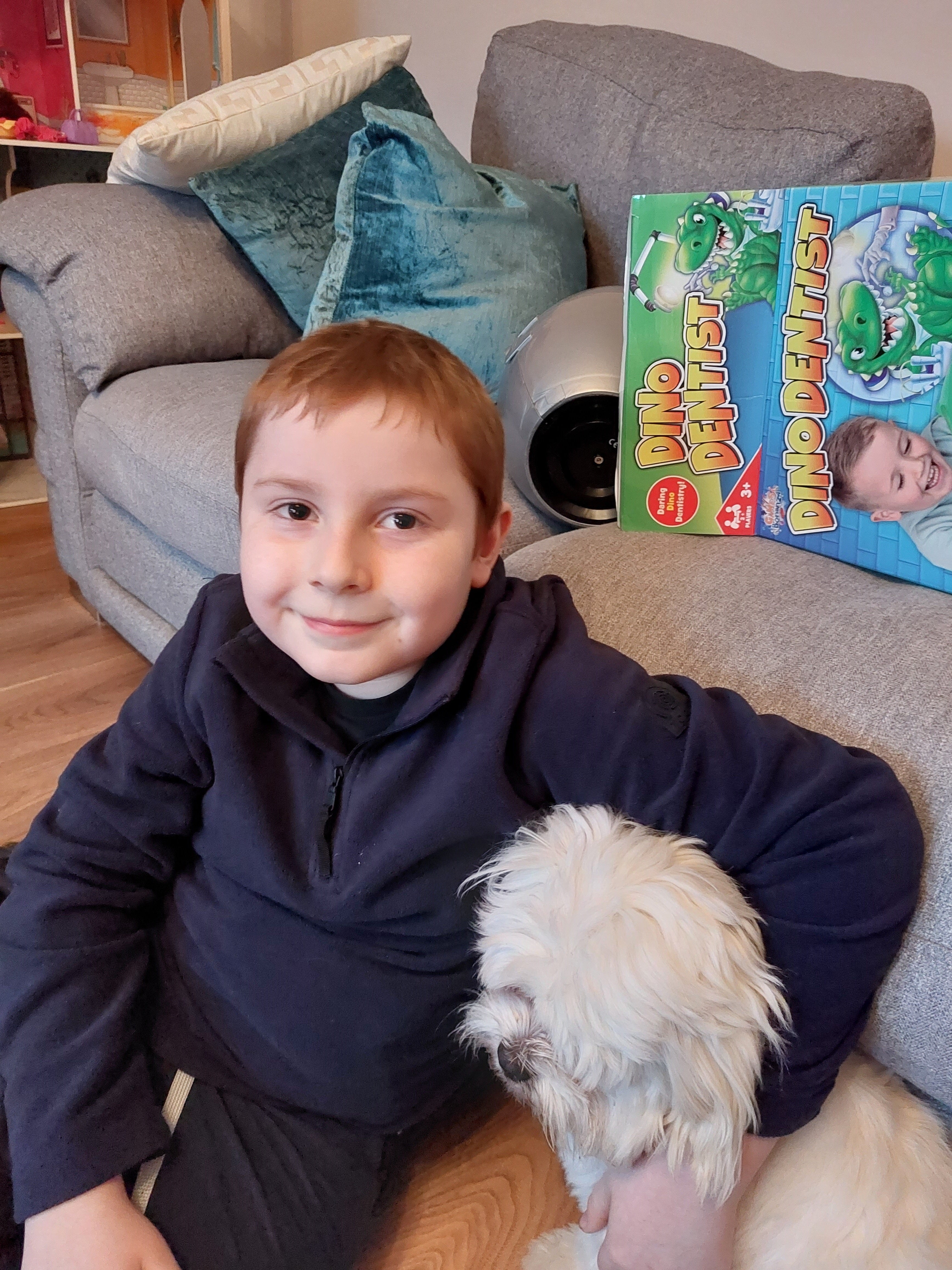 Bobby sitting on floor in front of as sofa cuddling a white dog