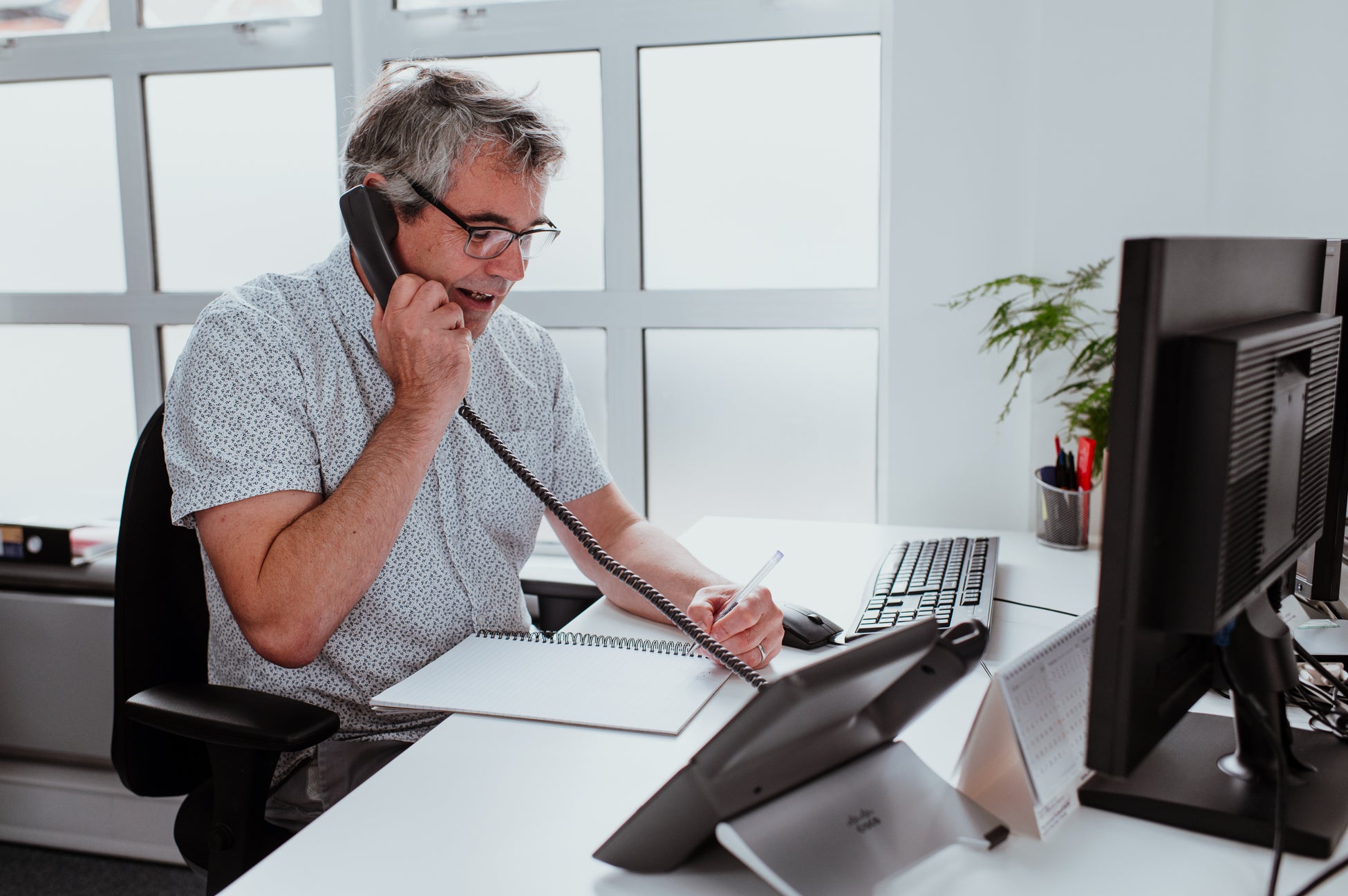 A man sat at a desk on the telephone