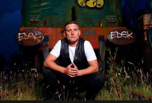 A serious looking man crouched down on grass at night